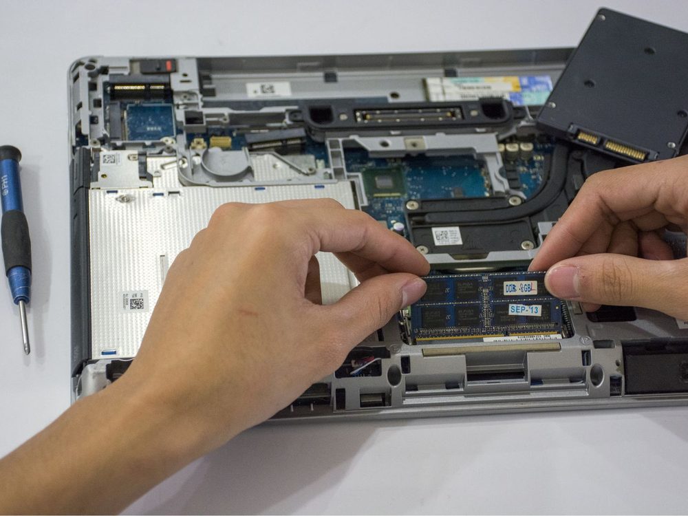 Hands installing a RAM module inside an open laptop