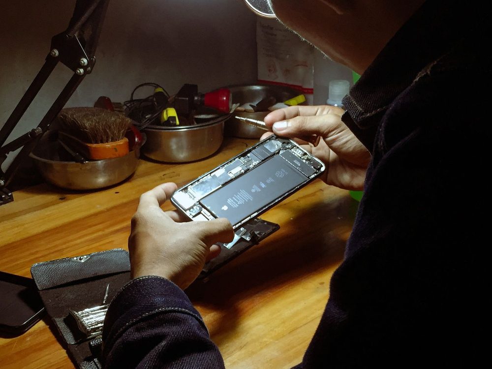 iPhone opened for repair on a wooden workbench under a desk lamp